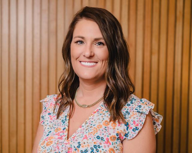 a woman in a floral shirt is smiling in front of a wooden wall .