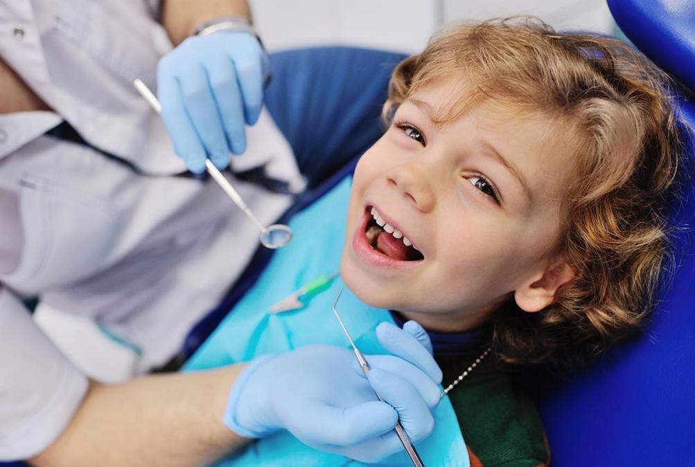 a young boy is sitting in a dental chair while a dentist examines his teeth .