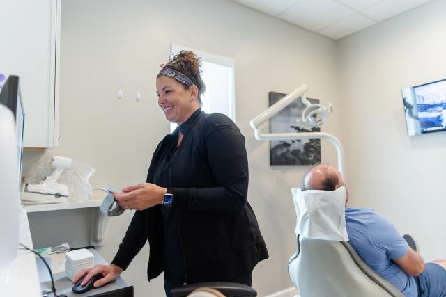 Smiling dental professional at a computer, patient in a dental chair.