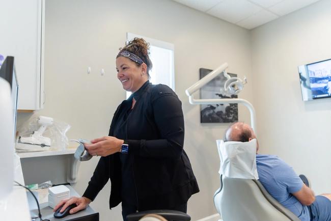 Smiling dental professional using a computer while a patient sits in a dental chair.