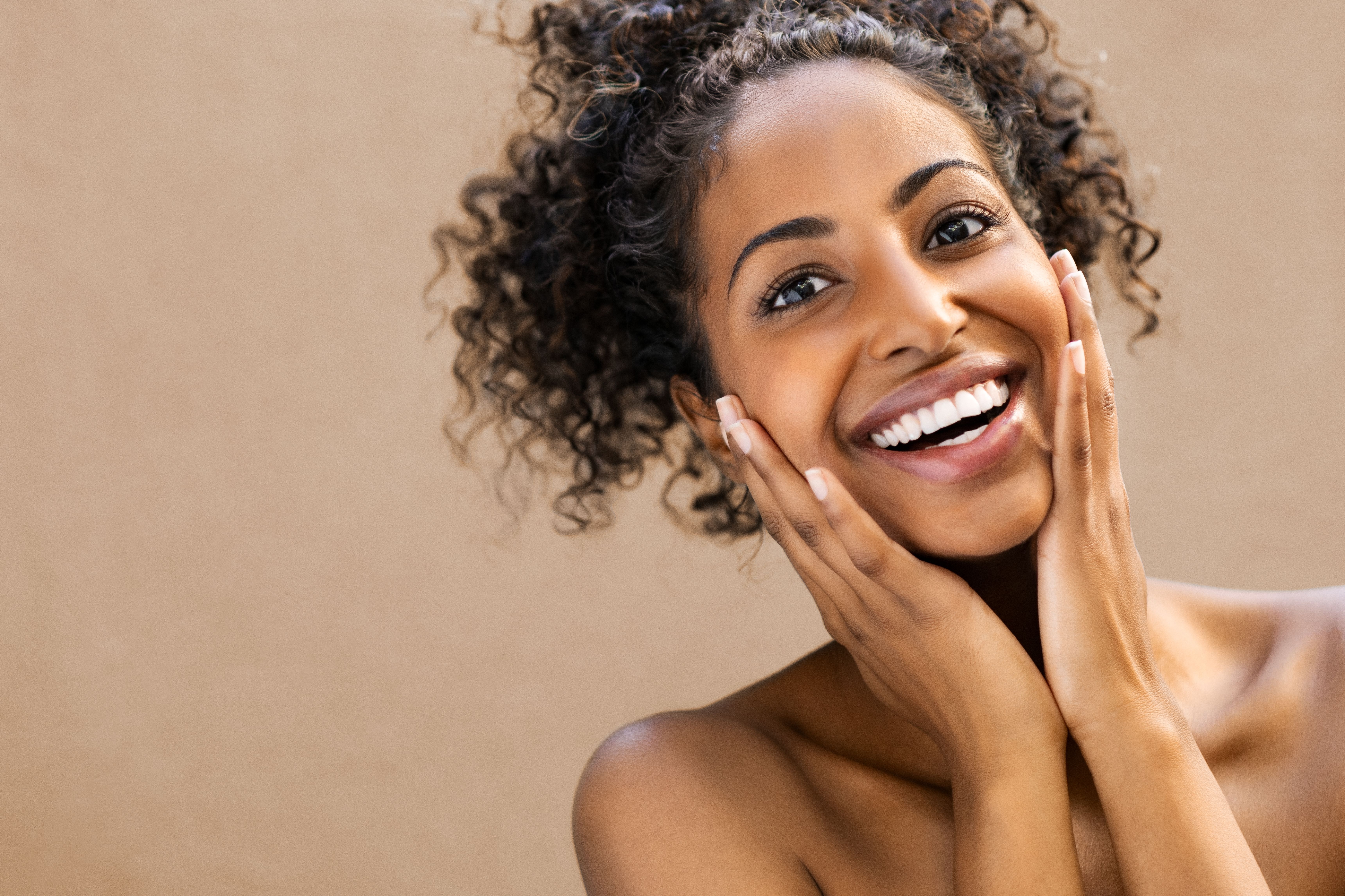 a woman with curly hair is smiling and touching her face.