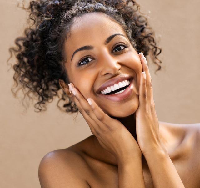 a woman with curly hair is smiling and touching her face .