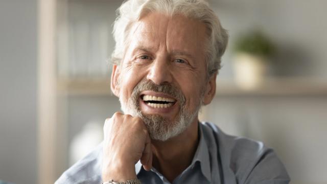 an older man with a beard is smiling with his hand on his chin .