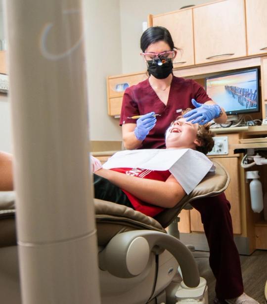 a female dentist is examining a young boy 's teeth in a dental chair .