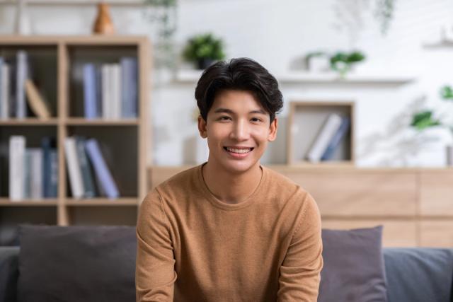 a young man is sitting on a couch in a living room smiling at the camera .