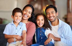 A smiling family of four, including a mother, father, son, and daughter, sitting together.