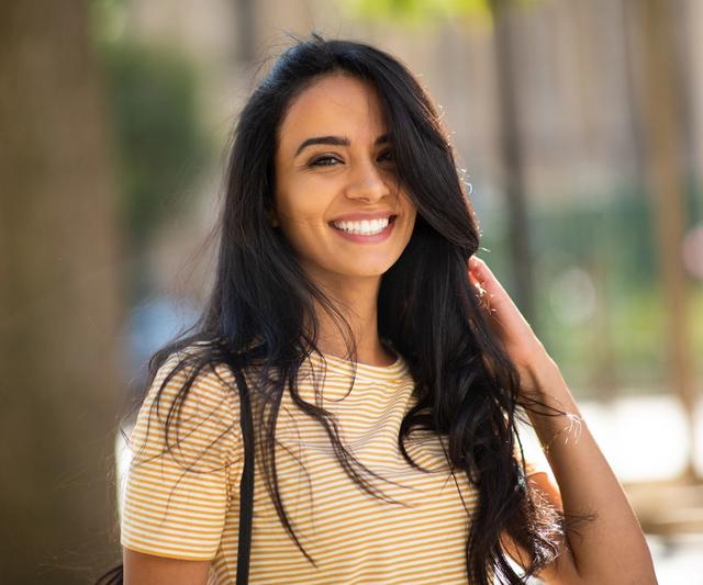 a woman in a yellow striped shirt is smiling and touching her hair .