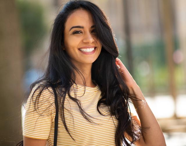 a woman in a yellow striped shirt is smiling and touching her hair .