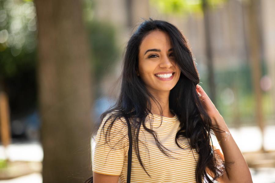 a woman in a yellow striped shirt is smiling and touching her hair .