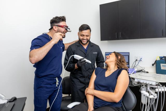 a woman is sitting in a dental chair while two dentists look at her teeth .