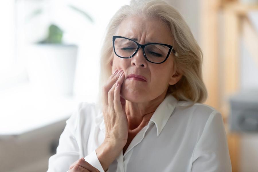 Woman with glasses grimacing and holding her cheek in pain.