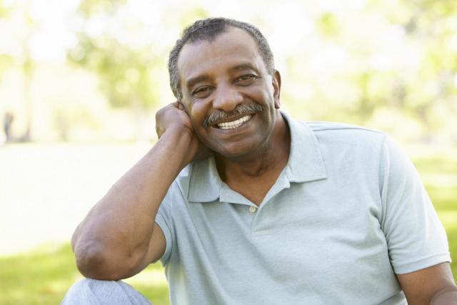 a man with a mustache is smiling with his hand on his chin .