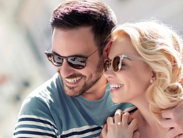 a man and a woman wearing sunglasses are hugging and smiling .