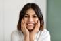 a woman is smiling with her hands on her face .
