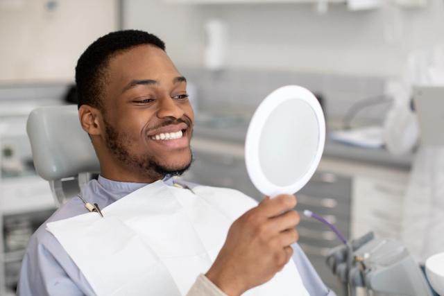 a man is sitting in a dental chair looking at his teeth in a mirror .