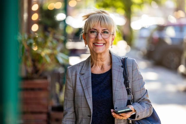 an older woman is walking down the street while holding a cell phone .