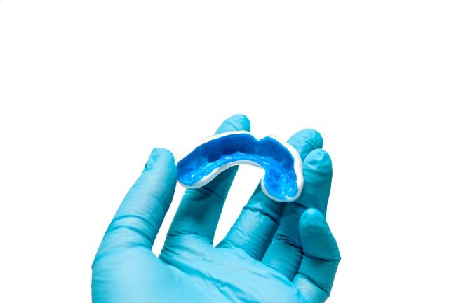 a person wearing blue gloves is holding a blue mouth guard .