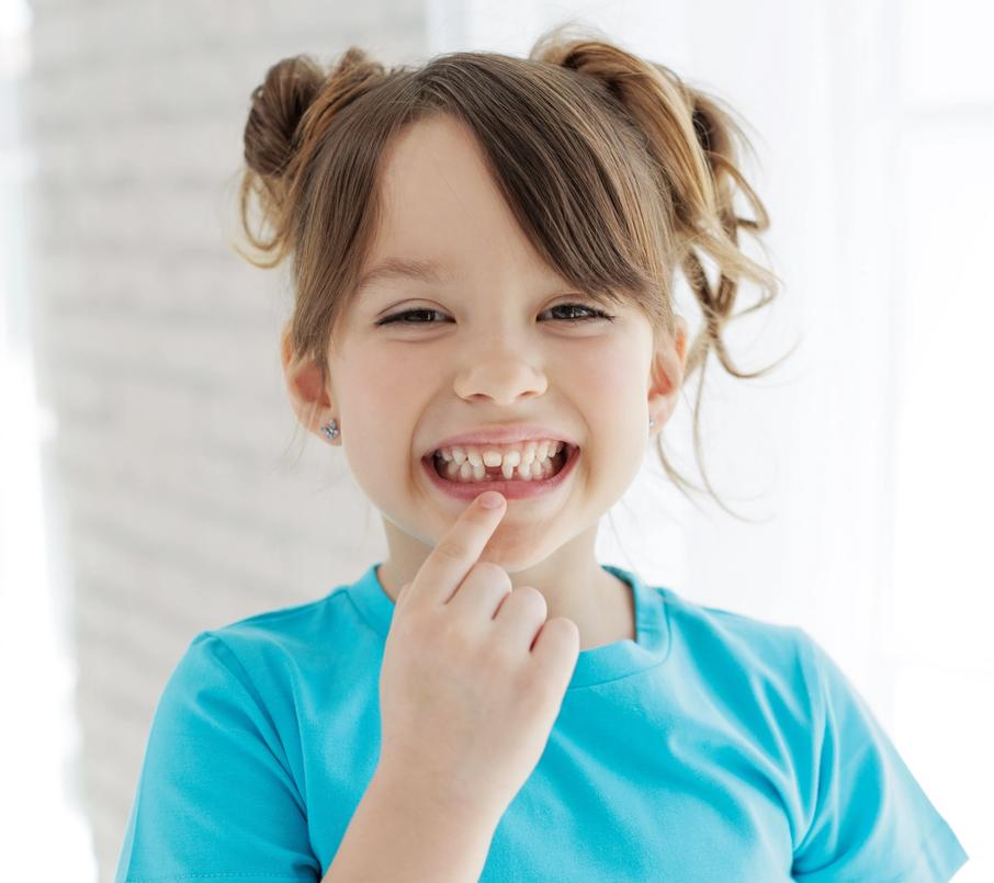 a little girl is pointing at her teeth and smiling .