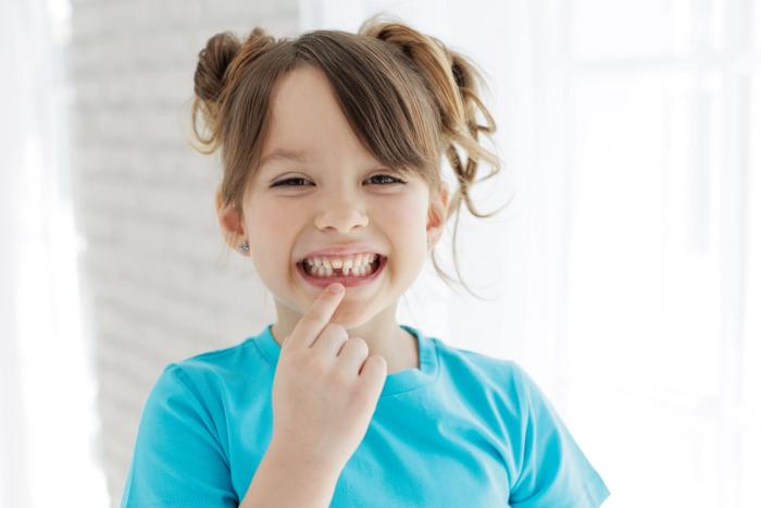 a little girl is pointing at her teeth and smiling .