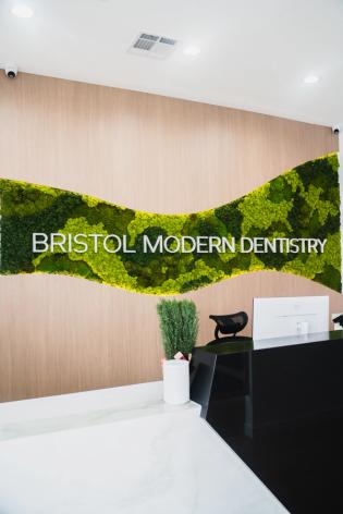 Modern reception area with "BRISTOL MODERN DENTISTRY" on a wavy green moss wall above a black desk.