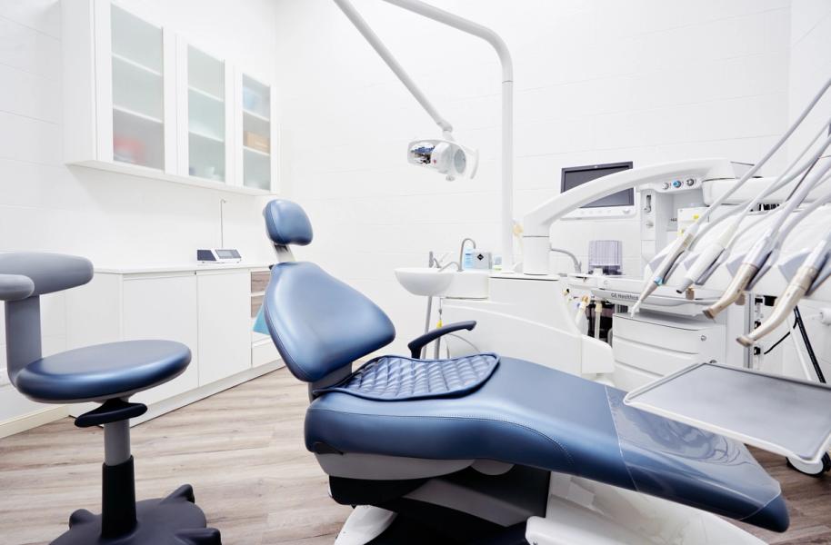 A modern dental examination room with a blue dental chair and white medical equipment.