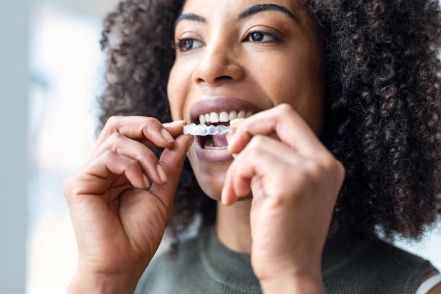 a woman is putting invisible braces on her teeth .