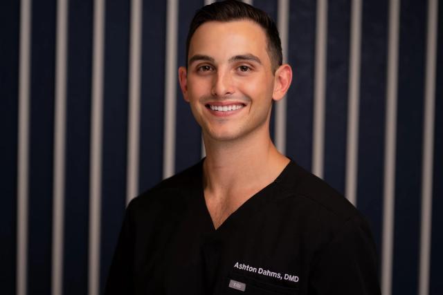 a young man in a black scrub top is smiling for the camera .