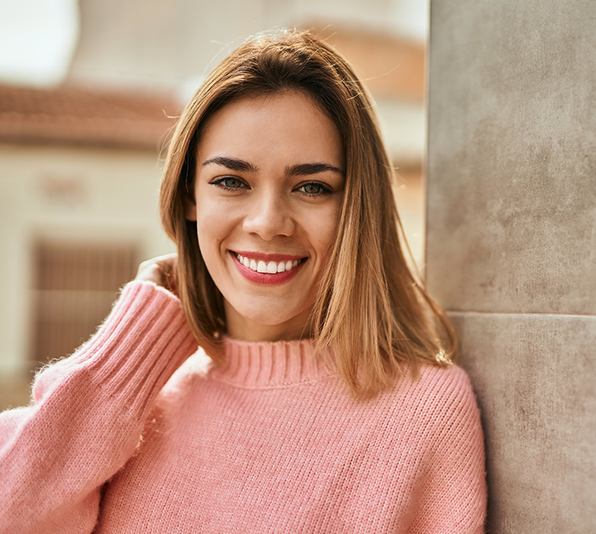 a woman in a pink sweater is leaning against a wall and smiling