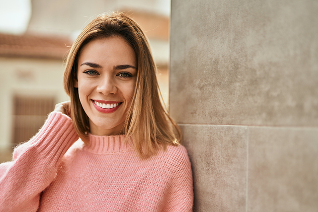 a woman in a pink sweater is leaning against a wall and smiling