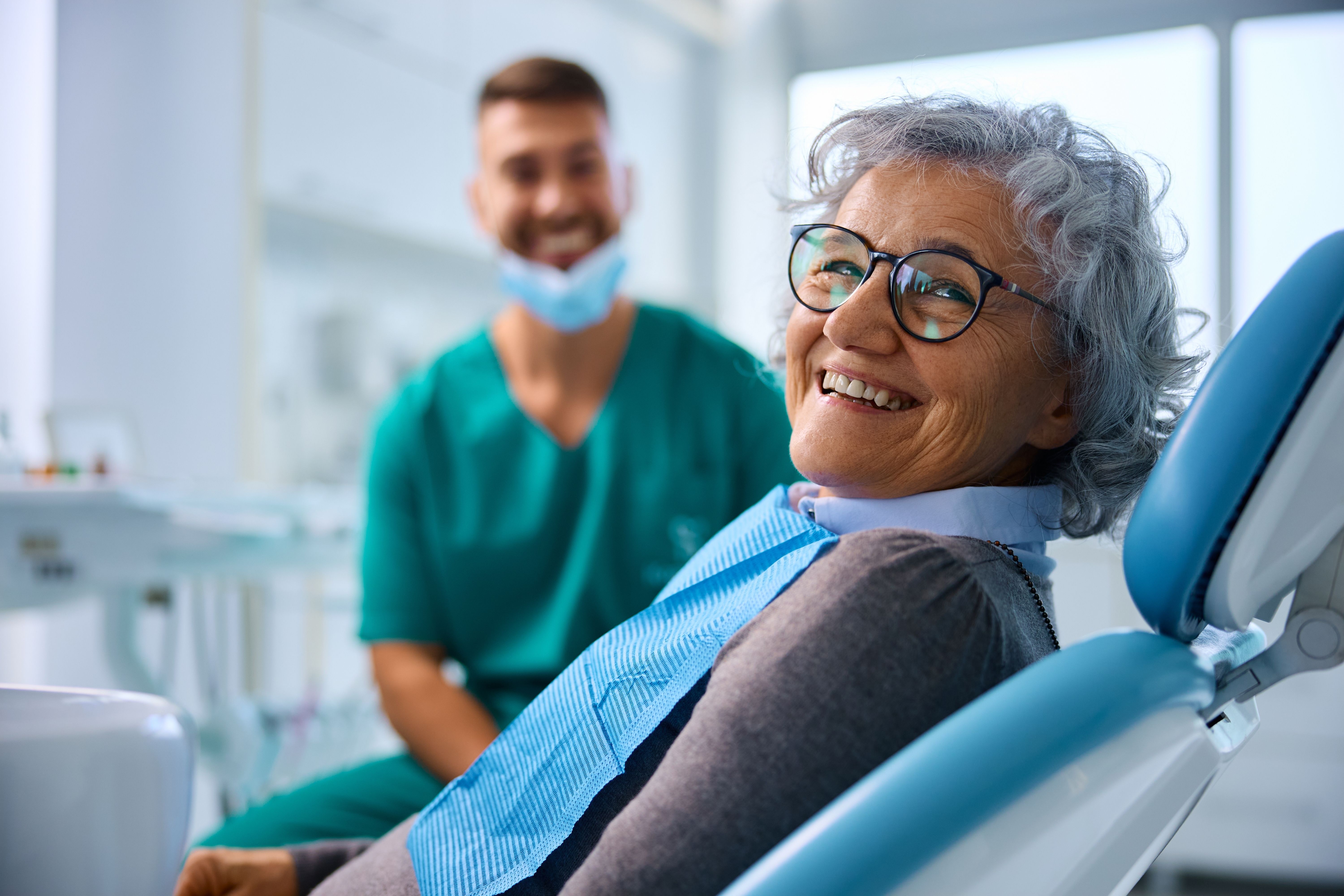 an elderly woman is smiling while sitting in a dental chair .