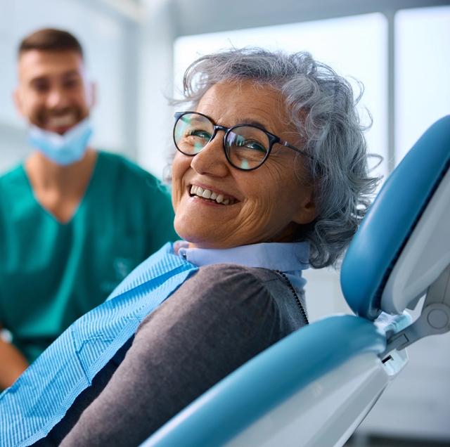 an elderly woman is smiling while sitting in a dental chair .