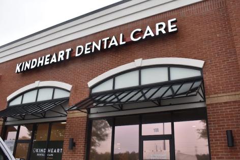 Kindheart Dental Care sign on a red brick building with arched windows and dark awnings.