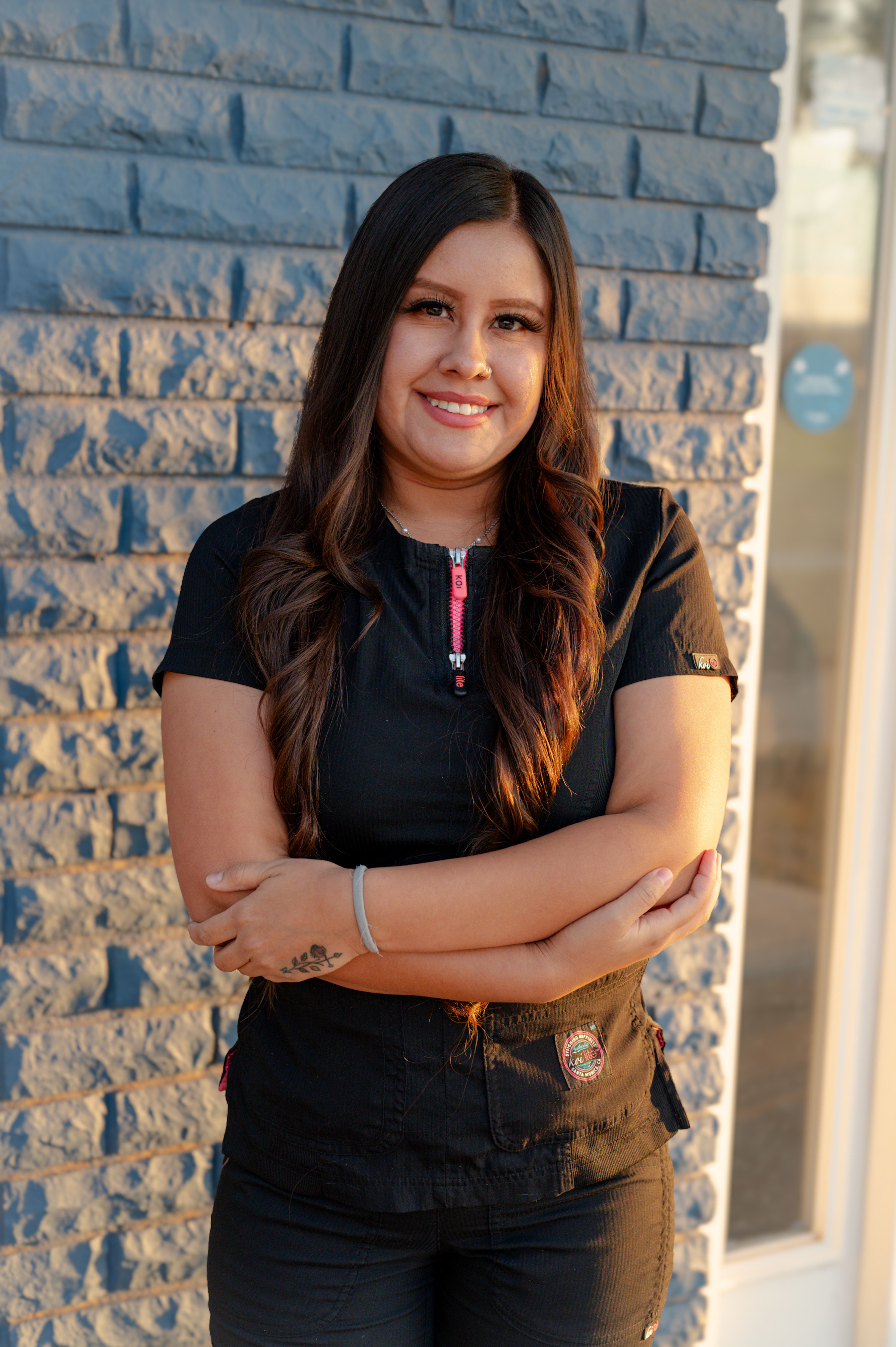a woman standing in front of a brick wall with her arms crossed