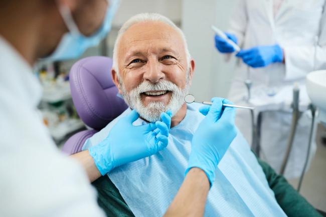 an elderly man is sitting in a dental chair while a dentist examines his teeth .