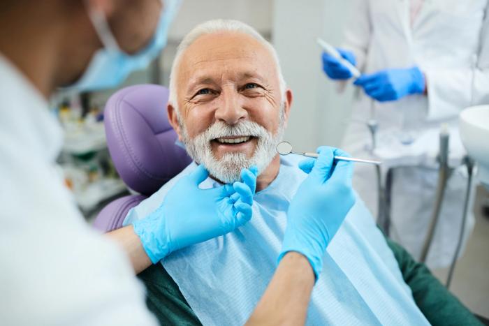 an elderly man is sitting in a dental chair while a dentist examines his teeth .