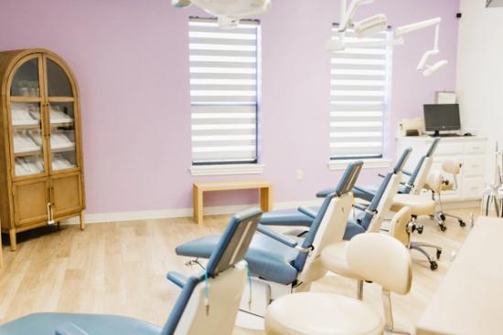 A dental examination room with purple walls, multiple light blue dental chairs, and equipment.