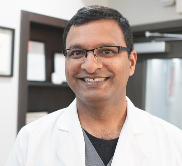 A smiling doctor in a white lab coat and glasses.