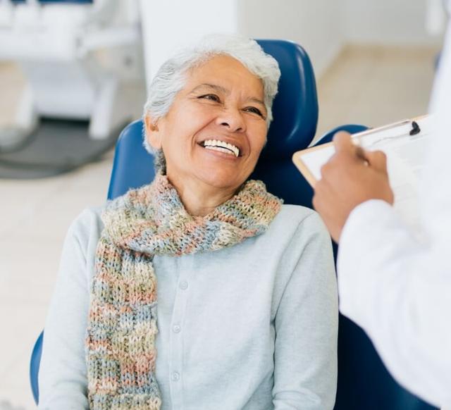 an elderly woman is smiling while sitting in a dental chair .