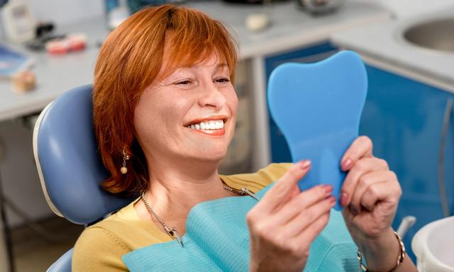 a woman is sitting in a dental chair looking at her teeth in a mirror .