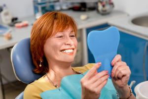 a woman is sitting in a dental chair looking at her teeth in a mirror .