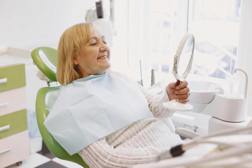 a woman is sitting in a dental chair looking at her teeth in a mirror .