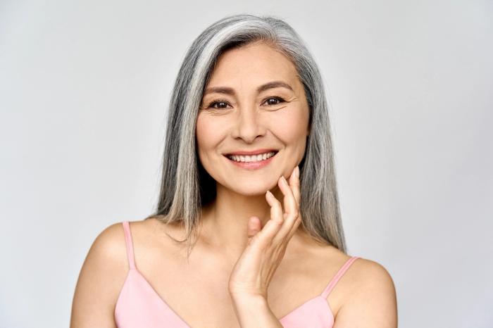 a woman with gray hair is smiling and touching her face .