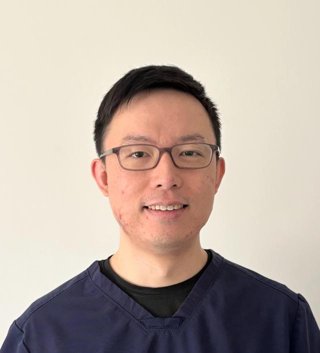 a man wearing glasses and a blue scrub top is smiling for the camera .