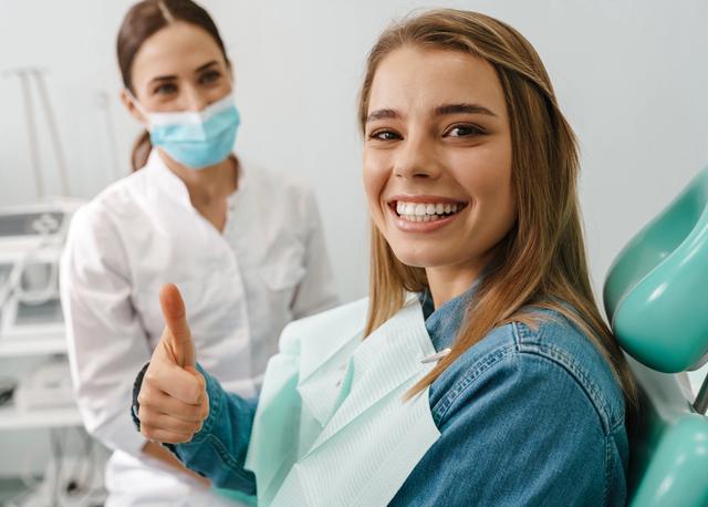 a woman is sitting in a dental chair and giving a thumbs up .
