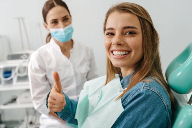 a woman is sitting in a dental chair and giving a thumbs up .