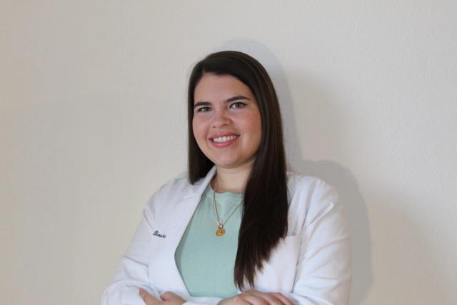 a woman in a white lab coat is smiling and standing with her arms crossed .