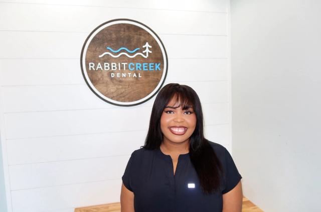 a woman is standing in front of a rabbit creek dental sign .