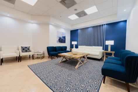 a waiting room with blue chairs , a couch , a coffee table and a rug .