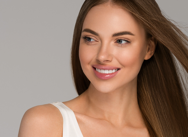 a woman with long hair is smiling and wearing a white tank top