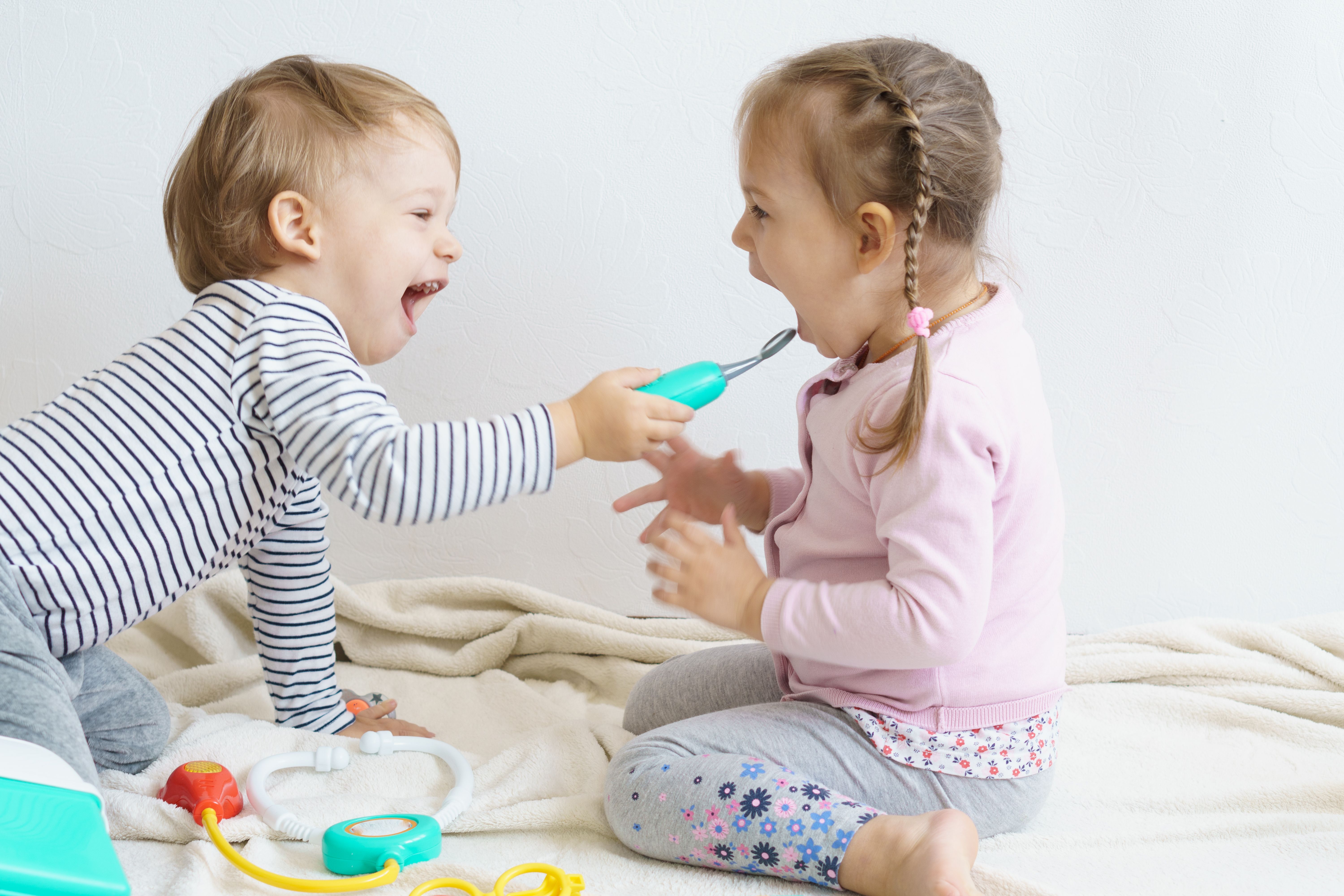 Two laughing children playing doctor with toy medical tools.